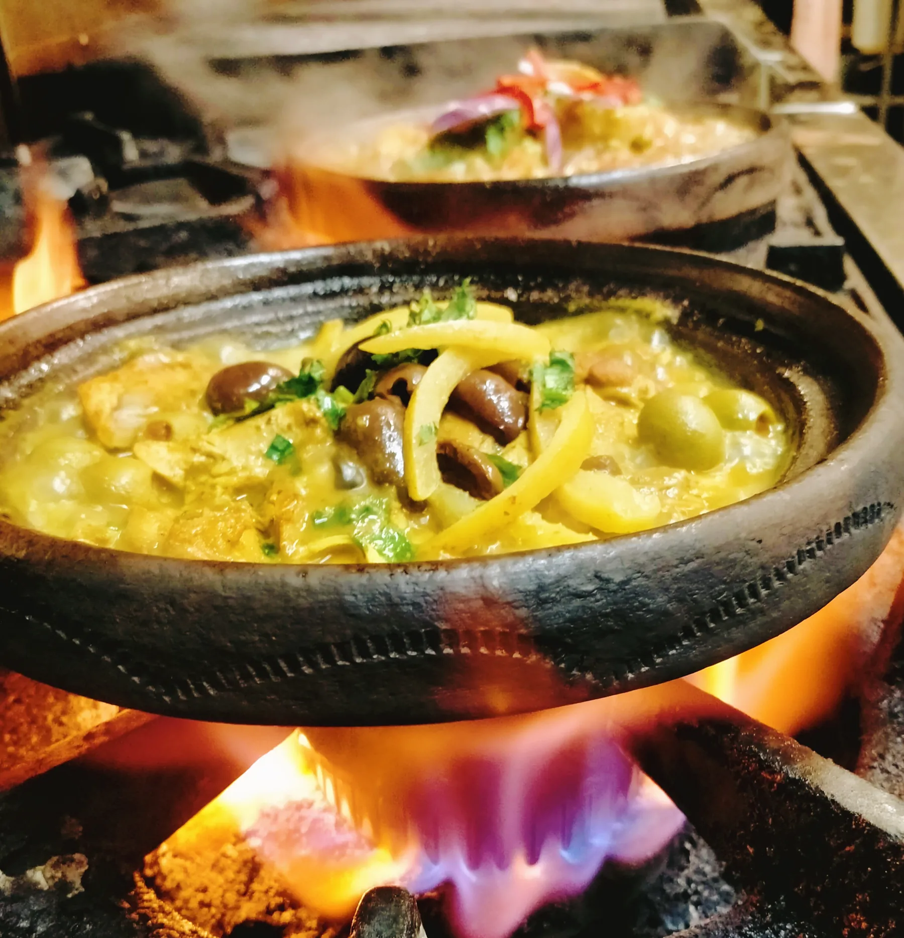 A clay tagine of chicken, olives and preserved lemon cooking over glowing coals